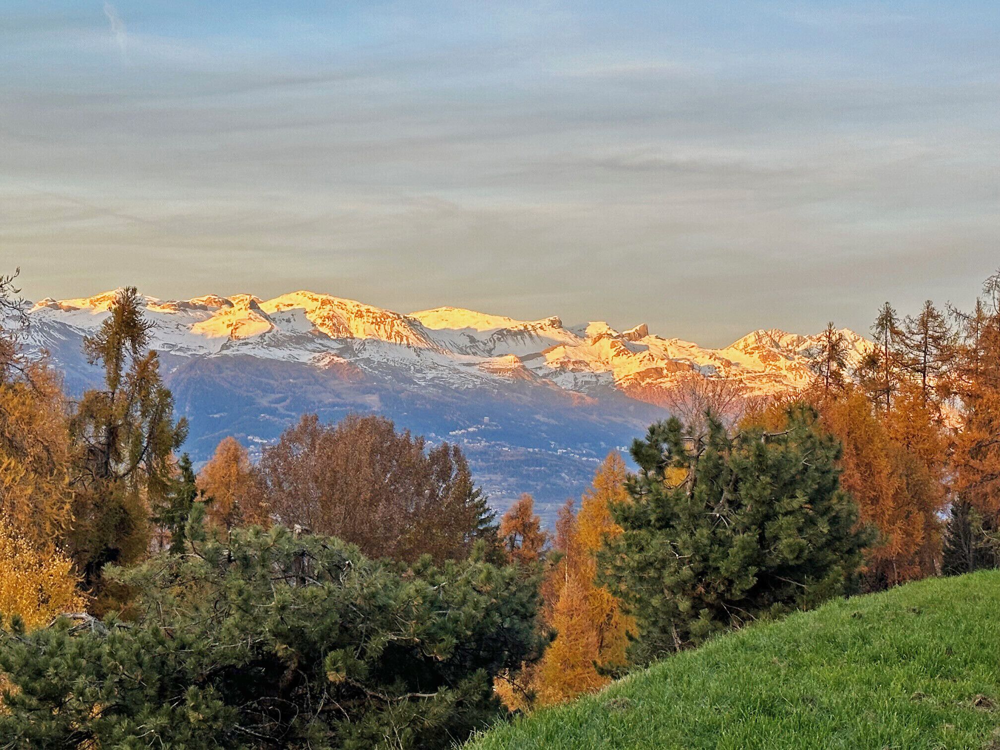 A mountainous landscape with snow-capped peaks and autumn-colored trees.