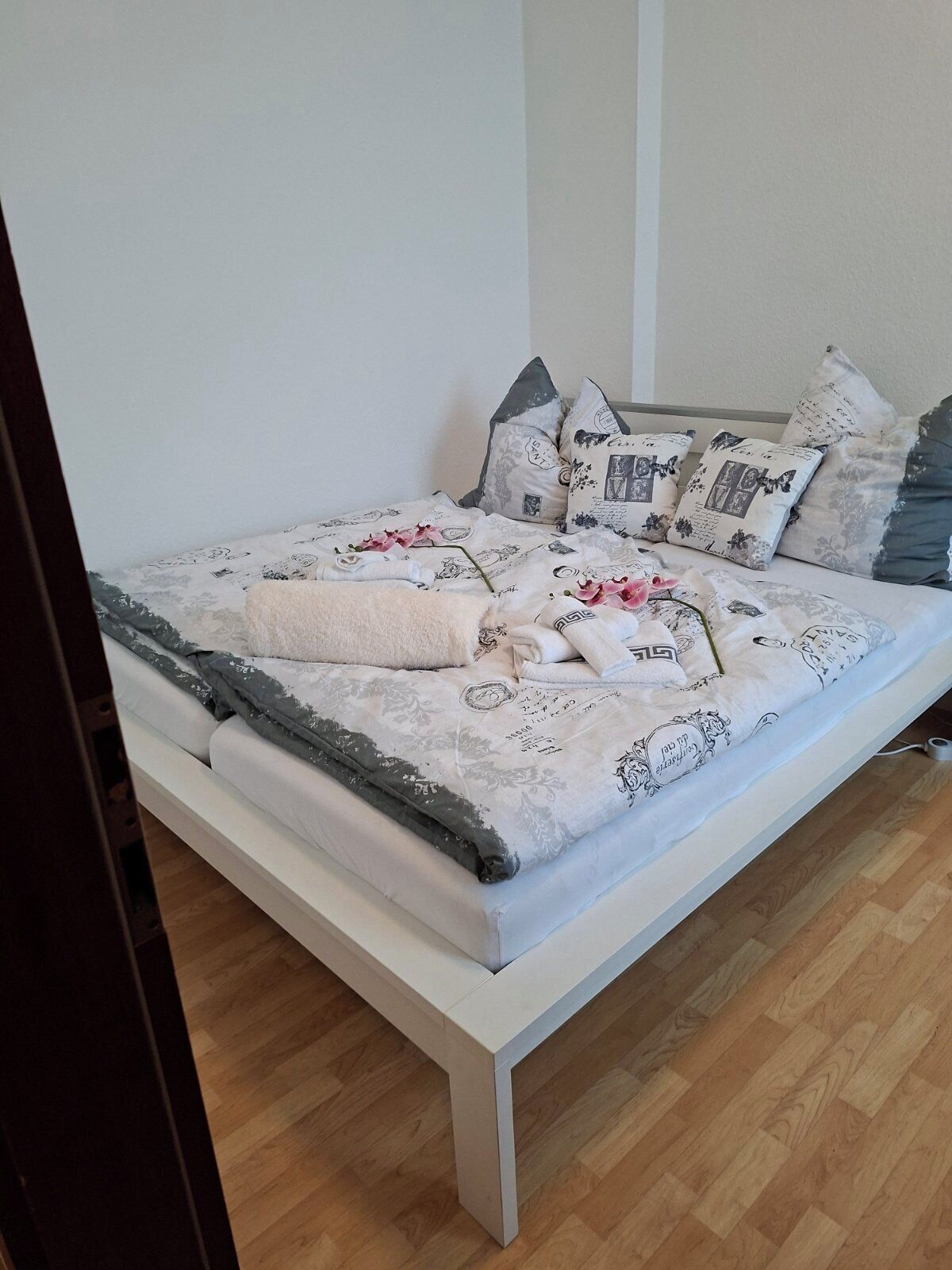 Un lit bien fait, avec une literie à motifs et des oreillers, un plancher en bois et un mur blanc.
