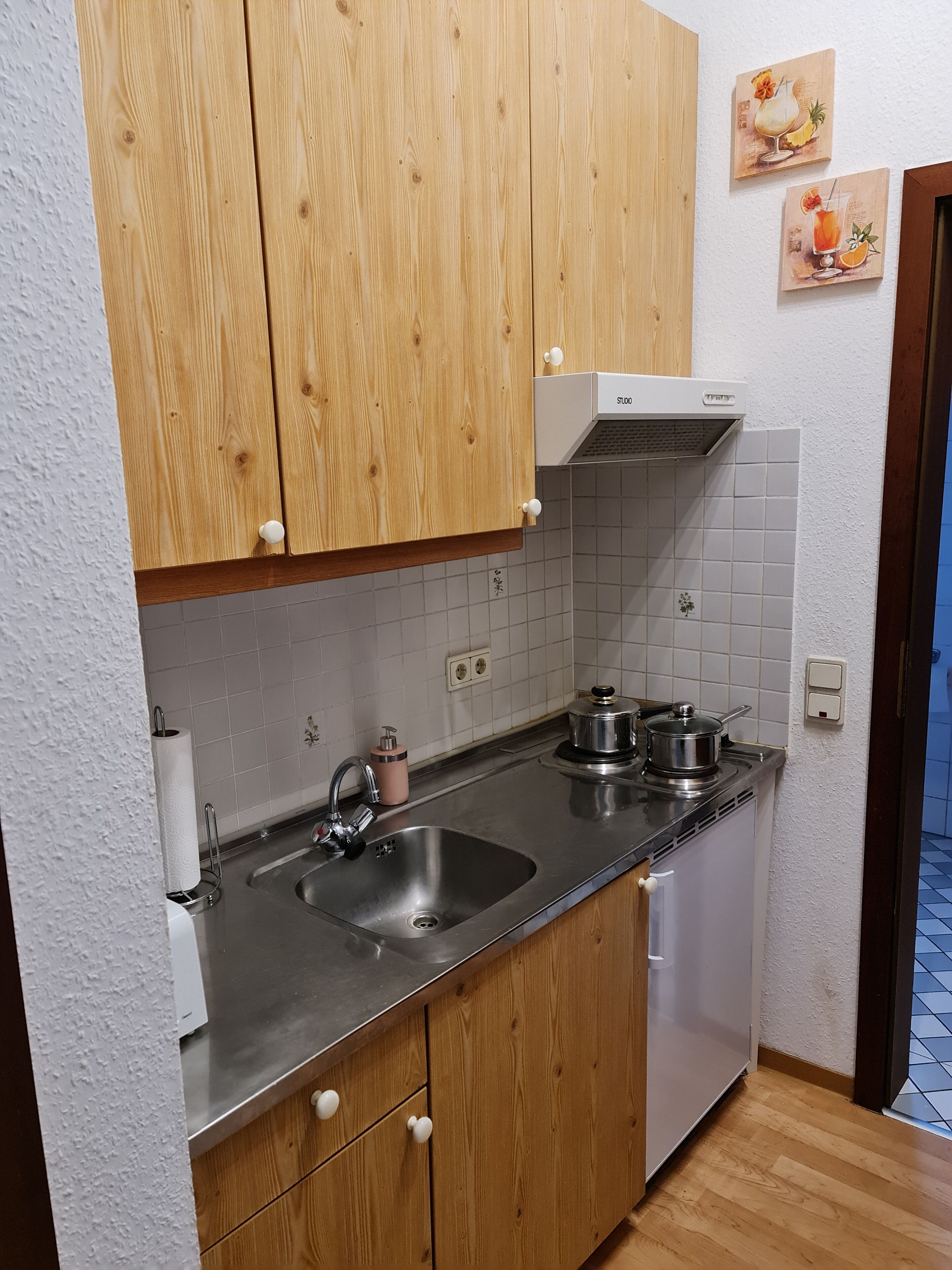 A kitchen with wooden cabinets, a stainless steel sink, and a small refrigerator.