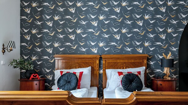 A double bed with a wooden headboard, two bedside tables, and a patterned wallpaper with white and gold birds. - Giselle Buda Castle (Budapest)