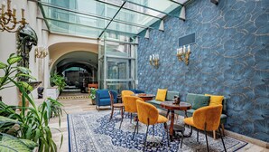 A modern interior with a glass ceiling, blue patterned walls, and a mix of blue and yellow furniture. - Giselle Buda Castle (Budapest)