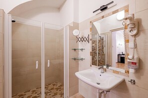 A bathroom with a glass-enclosed shower, a sink with a mirror above it, and a telephone on the wall. - Giselle Buda Castle (Budapest)