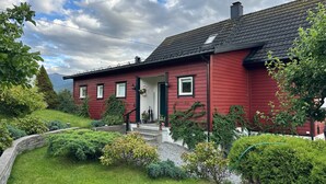 Una casa rossa con un portico, immersa in giardini curati e un cielo sereno.