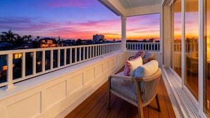Un balcone con vista sul tramonto, una sedia in vimini e una ringhiera.