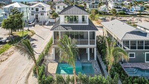 Una casa a due piani con piscina, circondata da palme e una spiaggia sabbiosa.