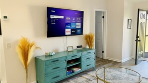 Un salon doté d’un meuble de télévision turquoise, d’un téléviseur à écran plat fixé au mur, d’une table basse en verre et d’un tapis à motifs.