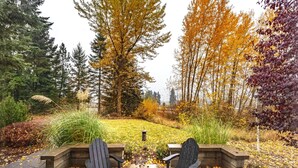 Une terrasse avec deux fauteuils Adirondack, une lanterne et un jardin aux couleurs automnales.