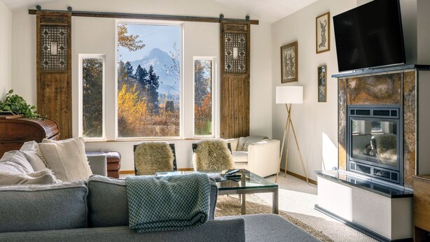 Un salon moderne comprenant un canapé, des fauteuils, une table basse, une cheminée et une grande fenêtre donnant sur une vue imprenable sur les montagnes.