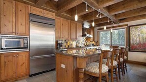 A kitchen with wooden cabinets, a stainless steel refrigerator, a microwave, and a bar area with stools. - Treetops 4e 3 Bedroom Condo (Avon)