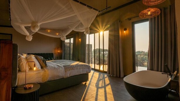 A bedroom with a large bed, a bathtub, and a view through the window.