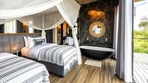 A bedroom with a bed, a large window, a bathroom with a bathtub, and a mirror.