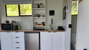 A modern kitchen with white cabinetry, a stainless steel dishwasher, a microwave, and a coffee machine. There is a window with a view of greenery outside. - Watts River Tiny - Hidden, but Close to Township (Healesville)