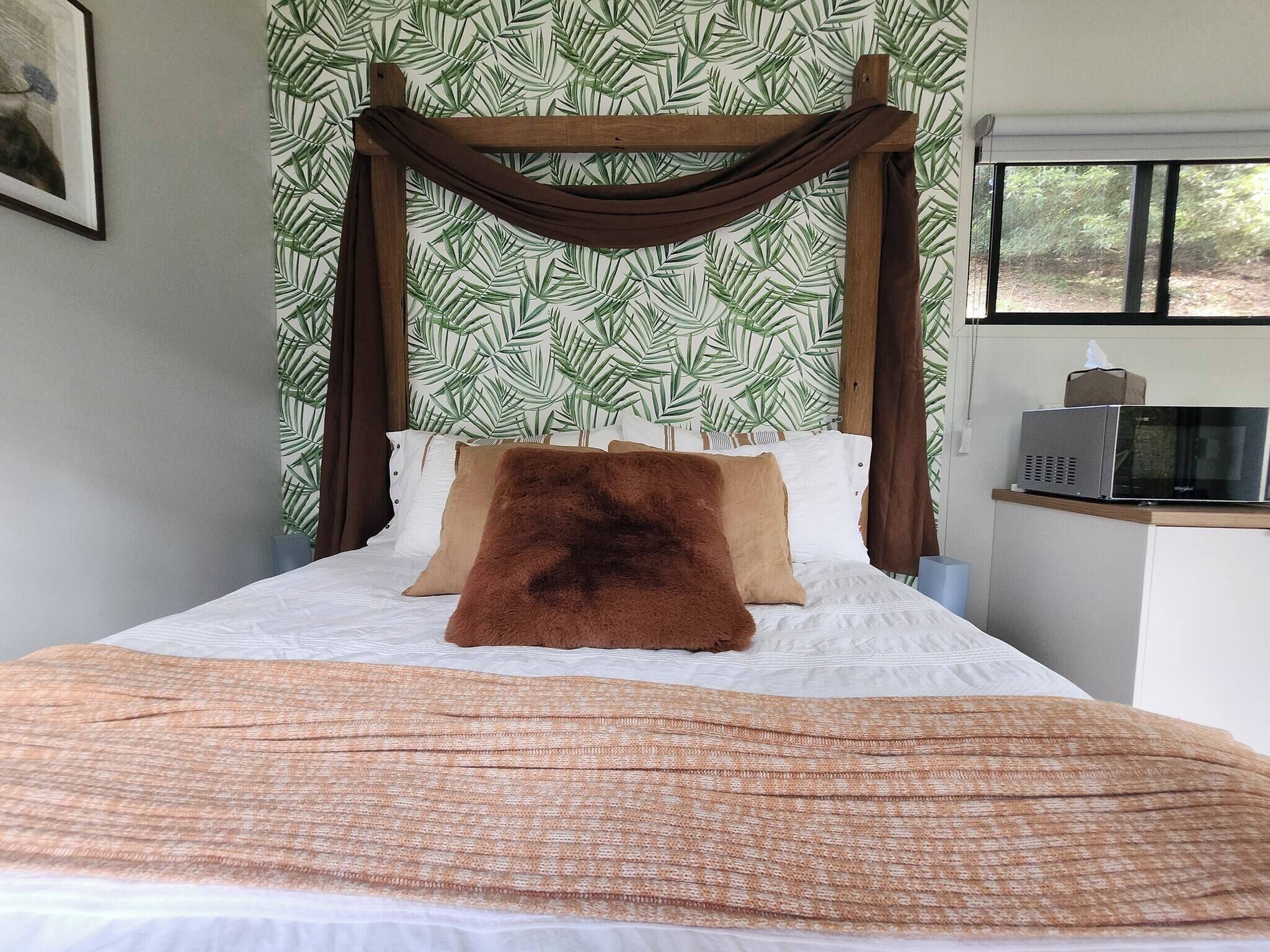 Uma cama com dossel, parede estampada e micro-ondas em bancada.