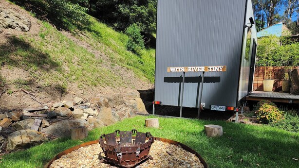 A circular gravel area with a metal structure, a grey building labeled "Watts River Tiny," and a wooden deck with potted plants. - Watts River Tiny - Hidden, but Close to Township (Healesville)