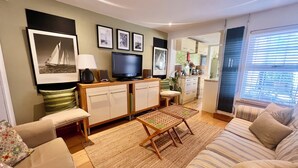 A living room with a sofa, a coffee table, a TV, and a kitchen area in the background.