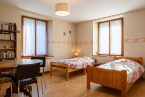 A bedroom with two wooden beds, a wooden desk, a chair, a bookshelf, and a window with curtains. - Apartment 'Le Gîte À Mamie' with Mountain View, Private Terrace and Wi-Fi (Orbey)