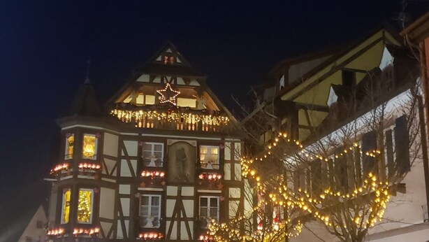 Un bâtiment traditionnel à colombages, orné d’une étoile sur le toit et entouré de guirlandes lumineuses.