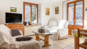 Un salon comprenant un téléviseur, un canapé, un fauteuil, une table et une fenêtre donnant sur un beau paysage.