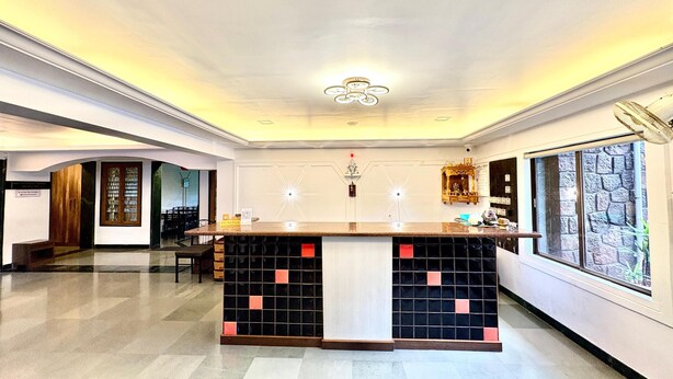 A spacious hotel lobby with a reception desk, a chandelier, and a large window with a stone facade. - Honey Bee - A Boutique Resort (Lonavala)