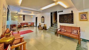 A hotel lobby with a reception desk, seating area with patterned sofas, a staircase, and a wall with a decorative panel. - Honey Bee - A Boutique Resort (Lonavala)