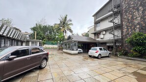 A residential area with two cars parked in a driveway, a covered carport, and a stone building with a spiral staircase. - Honey Bee - A Boutique Resort (Lonavala)