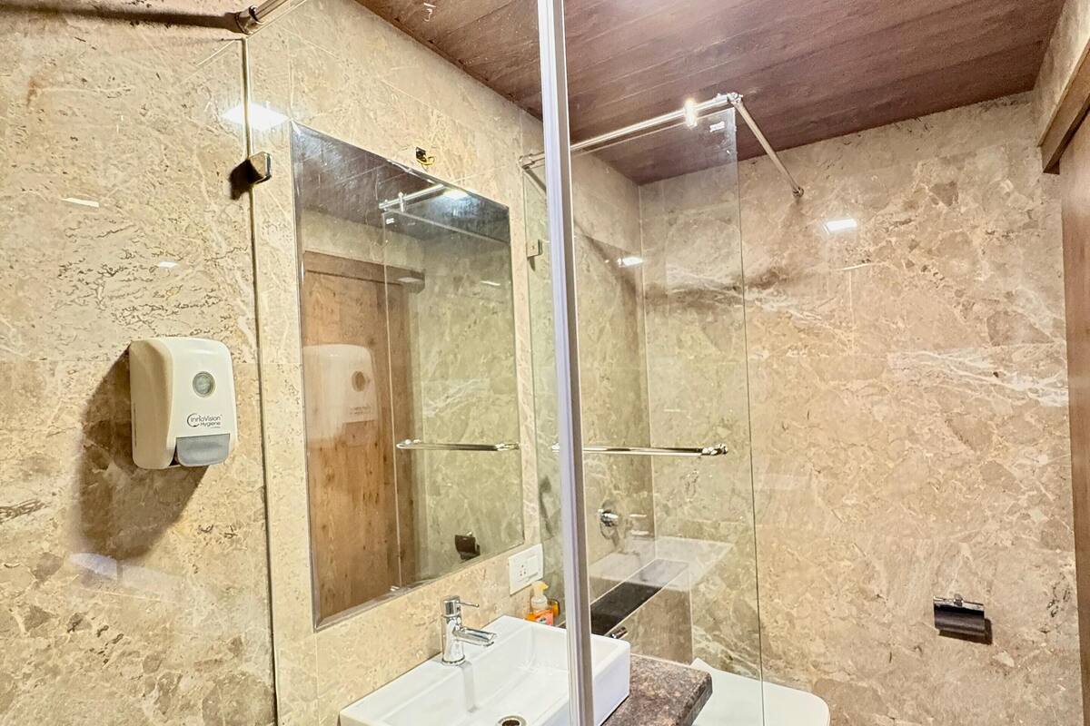 A bathroom with a marble wall, a glass-enclosed shower, a white sink, and a toilet.