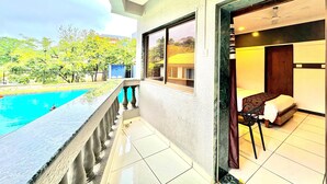 A hotel room with a balcony overlooking a swimming pool and a garden. - Honey Bee - A Boutique Resort (Lonavala)