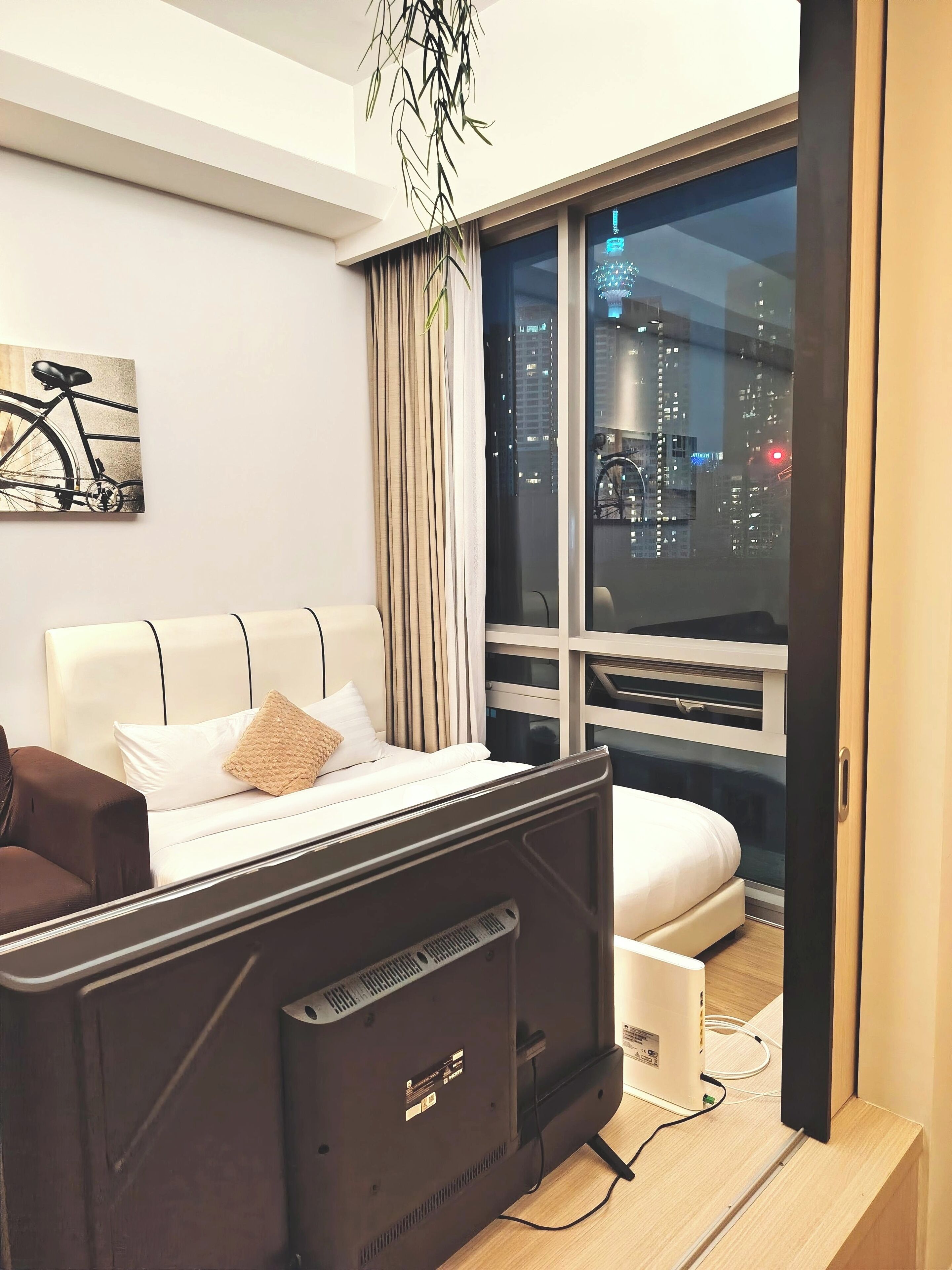 A modern hotel room with a bed, a desk, a chair, and a large window offering a city view.