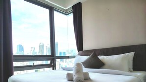 Une chambre d’hôtel avec un grand lit, une vue sur le paysage urbain à travers de grandes fenêtres et une vue dégagée sur les contours de la ville.