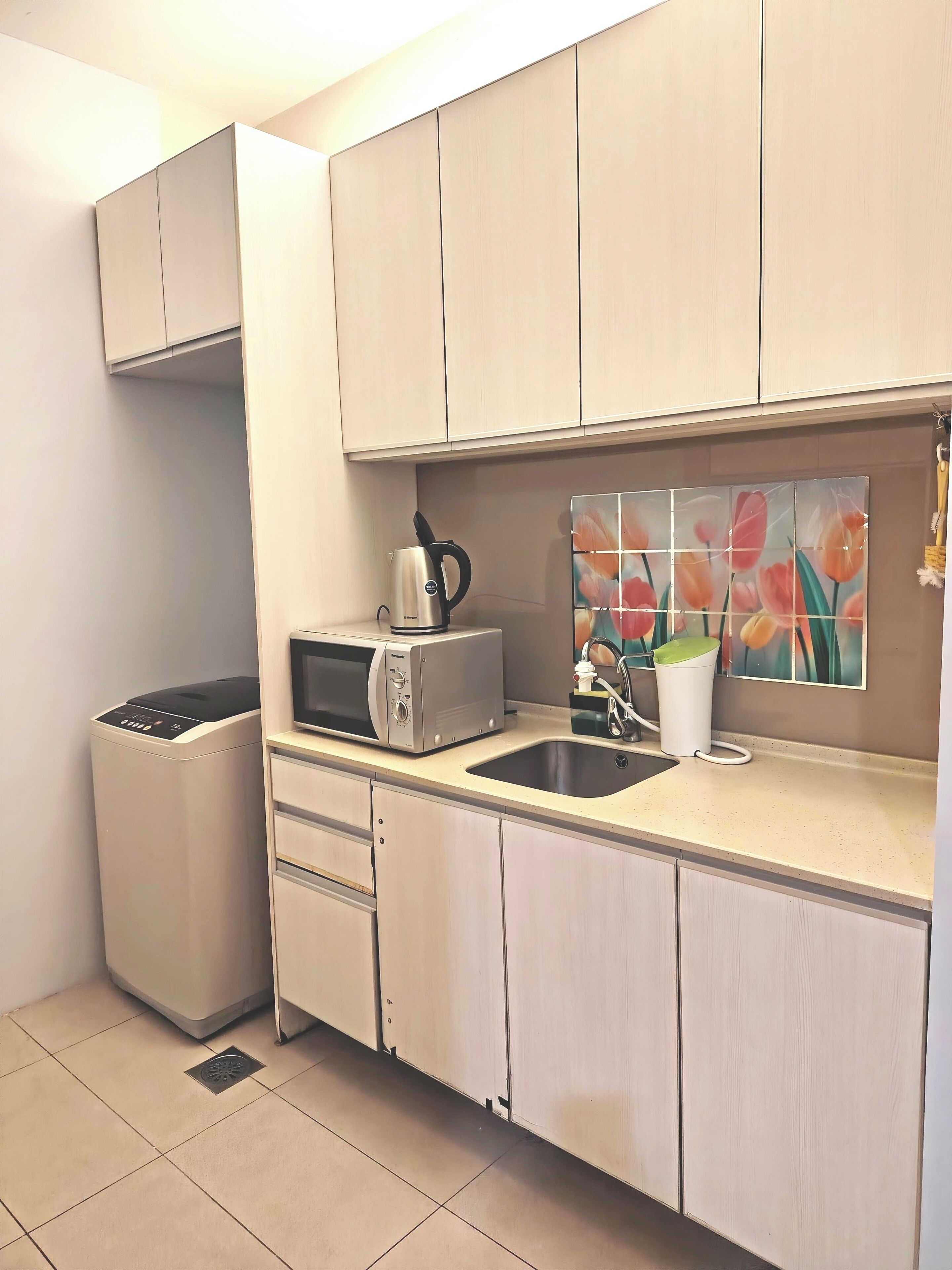 A compact kitchen with a microwave, toaster, and kettle on the countertop, a sink, and cabinets above.