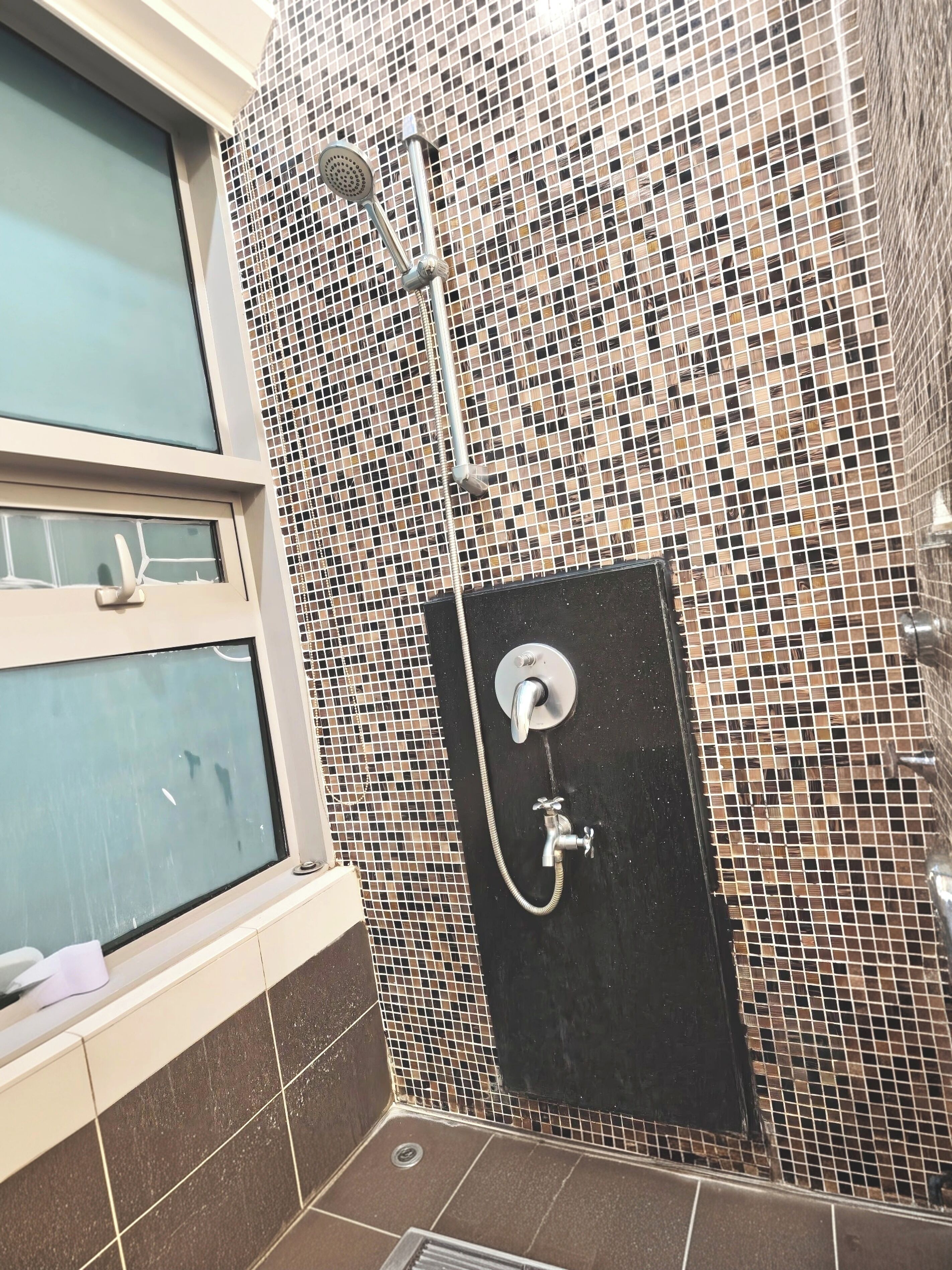 A shower area with a tiled wall, a window, and a black door.
