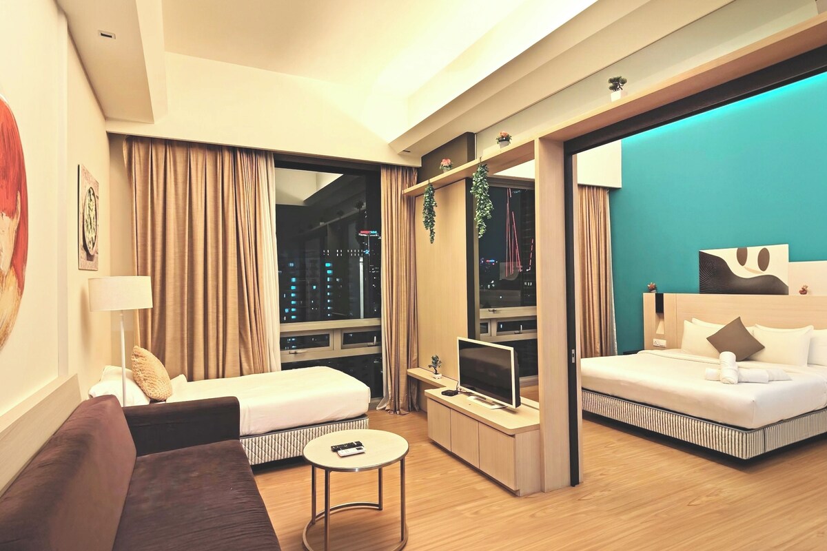 A modern hotel room with a sofa, a small round table, a TV, and a bed with a headboard.
