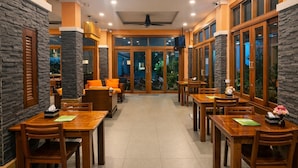Un restaurante con mesas y sillas de madera, paredes de piedra y ventanas amplias.