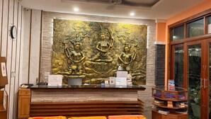 Zona de recepción con una gran estatua de Buda, un mostrador de recepción y un área de descanso con cojines naranjas.