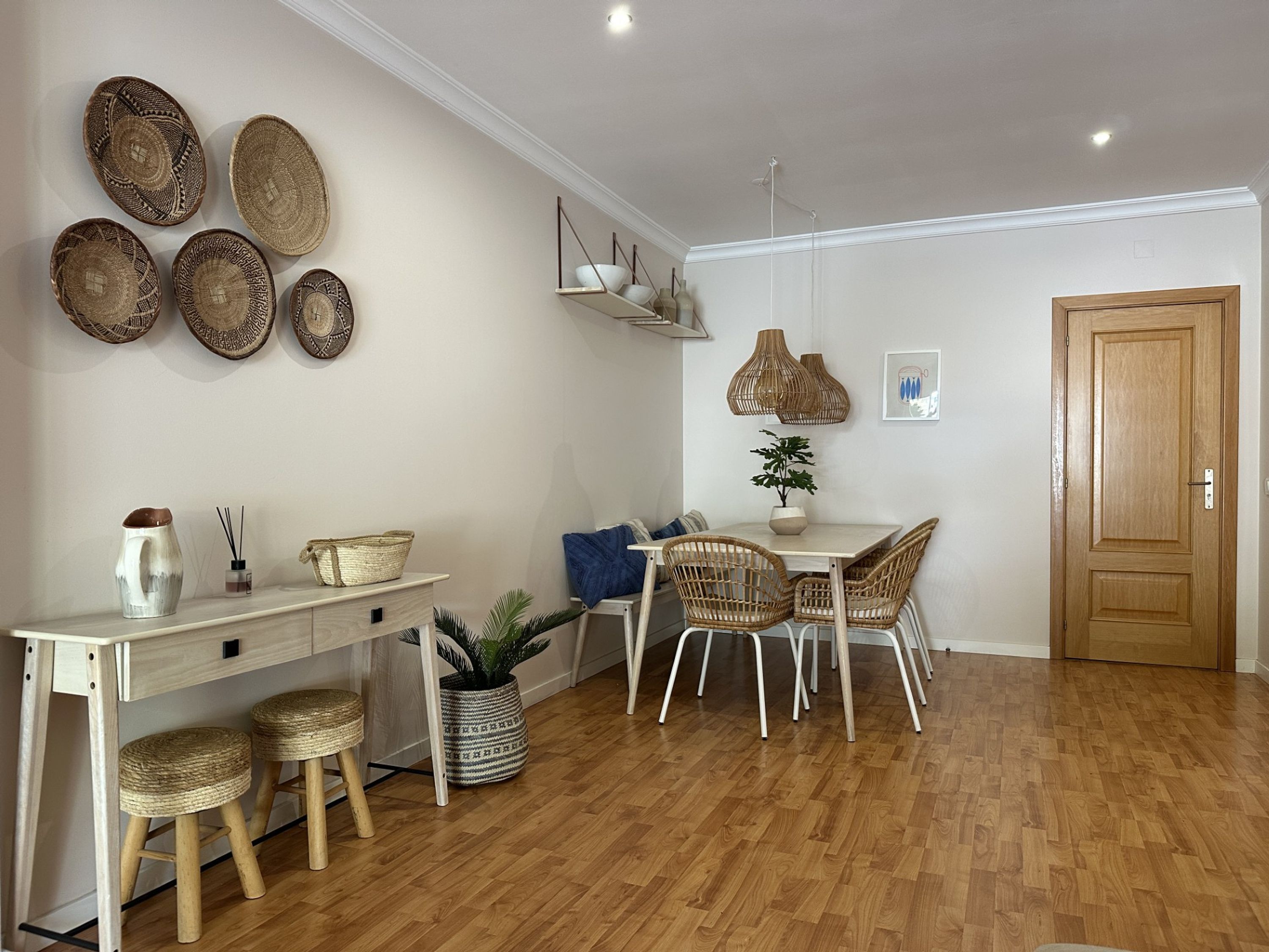 Un comedor con una mesa de madera, sillas de mimbre y una planta en maceta.