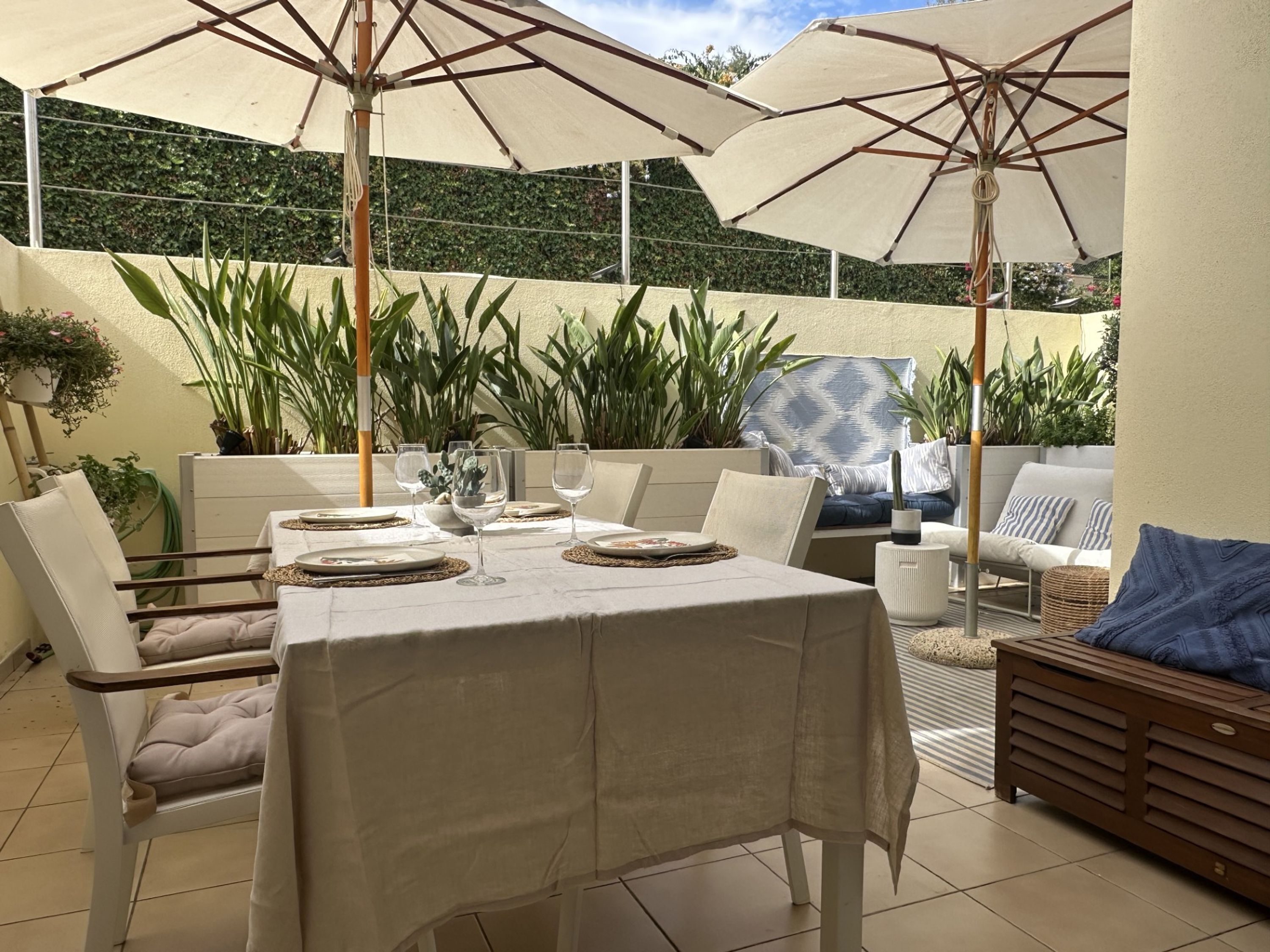 An outdoor patio with a table set for dining, surrounded by chairs and large umbrellas.