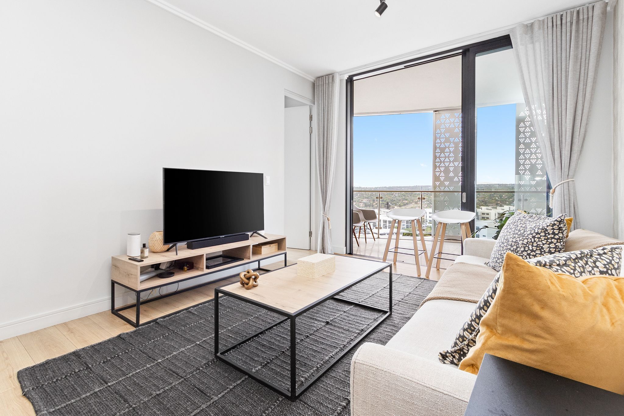 A modern living room with a flat-screen TV, a wooden coffee table, and a sofa with decorative pillows.