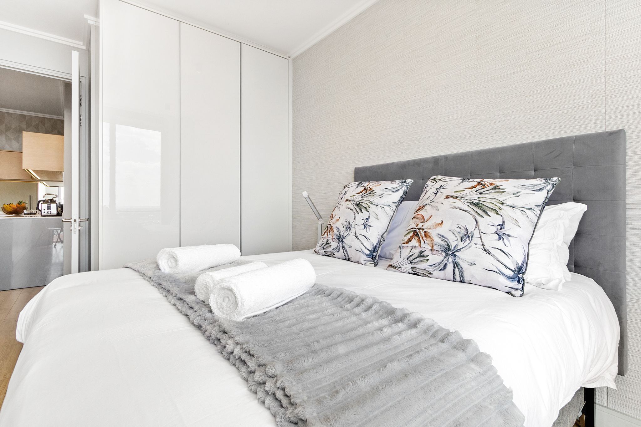 A modern hotel room with a neatly made bed, a grey rug, and floral pillows.