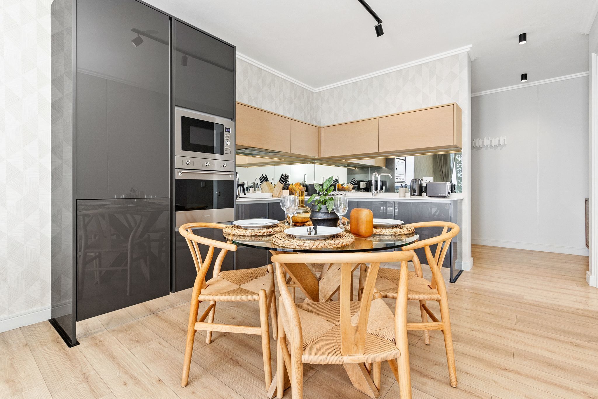 Una cocina moderna con armarios oscuros, una isla central y un comedor con sillas de mimbre y una mesa de vidrio.