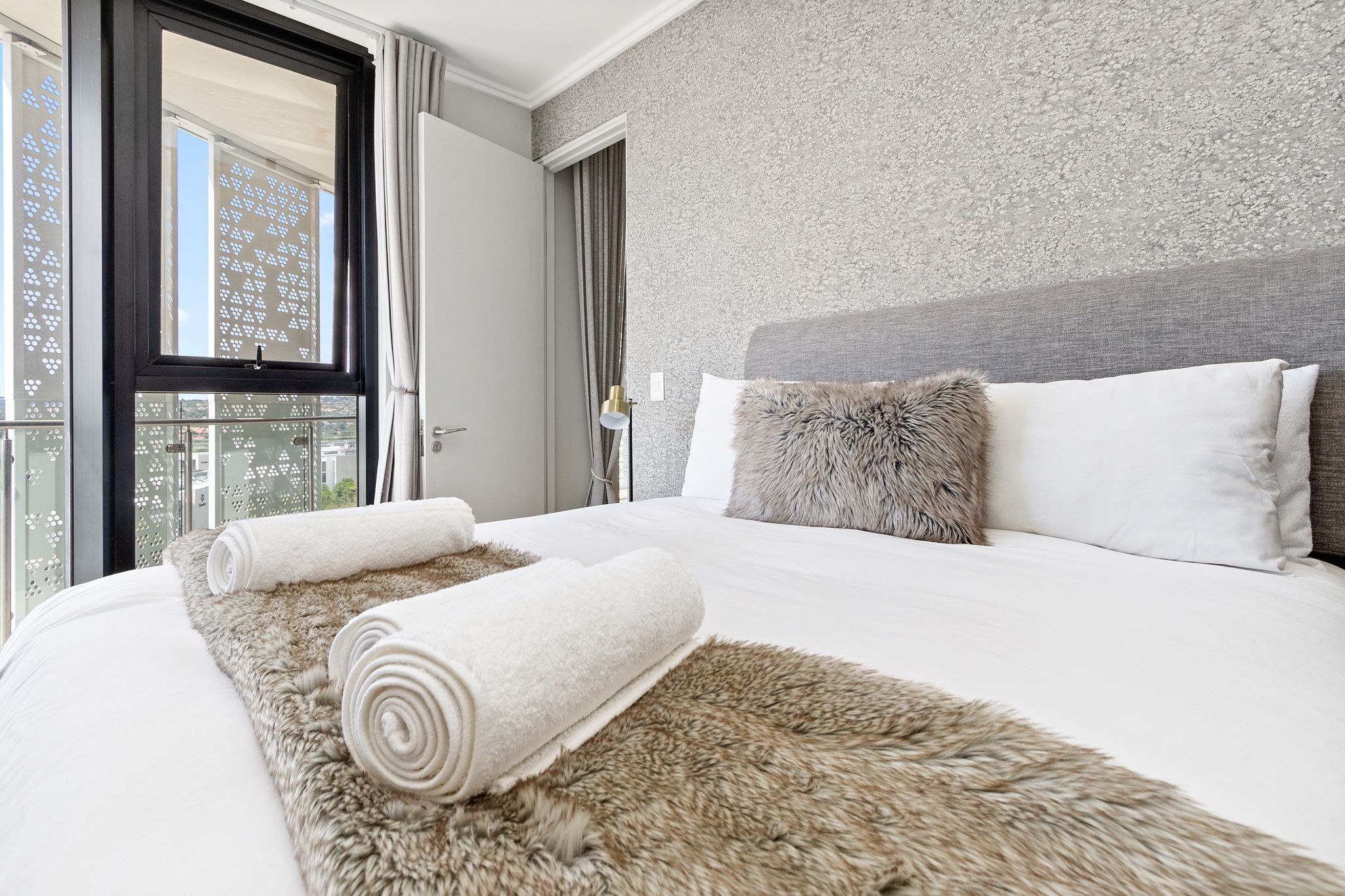 Een hotelkamer met een groot bed, een bont plaid en uitzicht op een gebouw door een raam.