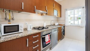 Een moderne keuken met houten kastjes, een magnetron, fornuis, oven en een wasmachine.