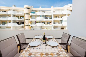 Un tavolo da pranzo apparecchiato con piatti, posate e una bottiglia di vino, con vista su un moderno edificio residenziale con balconi.
