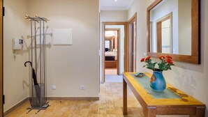 Een hal met een houten bankje, een vaas met bloemen, een metalen paraplu standaard en een spiegel aan de muur.