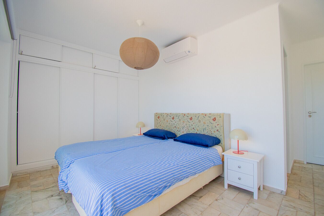 Una camera da letto con un letto, due comodini, una lampada a sospensione e un condizionatore d'aria.