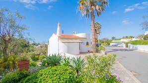 A white building with a red-tiled roof, surrounded by lush greenery and a palm tree. - 115 Vale do Milho - Vista do Mar (Lagoa)