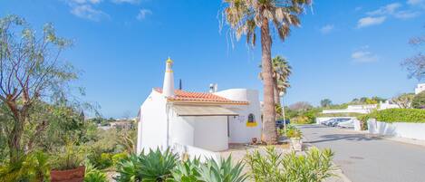 A white building with a red-tiled roof, surrounded by lush greenery and a palm tree.