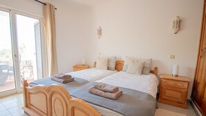 A bedroom with a wooden bed, two bedside tables, and a sliding glass door leading to a patio. - 115 Vale do Milho - Vista do Mar (Lagoa)