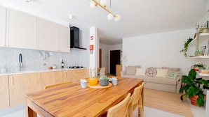 A modern kitchen with wooden cabinets, a dining table, and a living area with a sofa and plants. - Casa Flor do Mar in Carvoeiro (Lagoa)