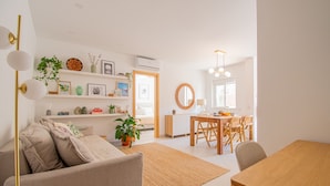 A modern living room with a sofa, a dining table, and a kitchen area in the background. - Casa Flor do Mar in Carvoeiro (Lagoa)
