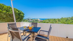 Une terrasse avec une table et des chaises, une table dressée avec une carafe et des verres, et une vue sur la mer et les bâtiments au loin.